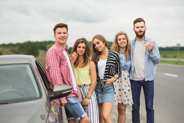 Portrait of young friends standing near the car on road