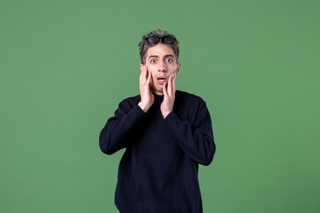 Portrait of young genius man dressed casually with surprised expression in studio shot on green surface