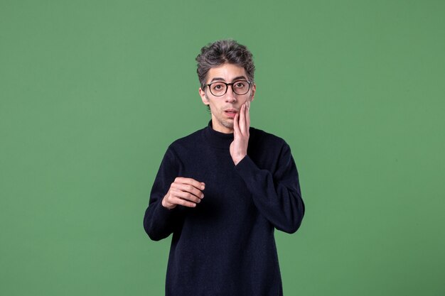 Portrait of young genius man dressed casually with surprised expression in studio shot on a green wall