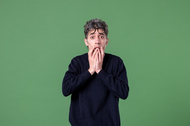 Portrait of young genius man dressed casually with surprised expression in studio shot on green wall