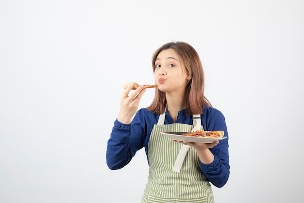 Портрет молодой девушки в фартуке, едят пиццу на белом