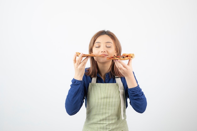 Ritratto di giovane ragazza in grembiule che mangia pizza su bianco