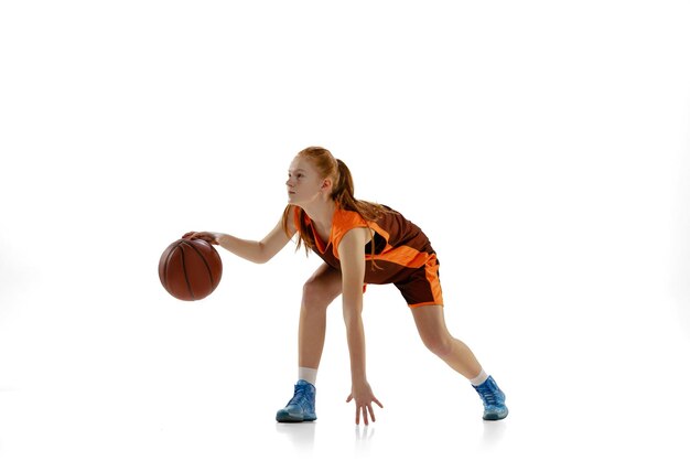 Portrait of young girl basketball player training dribbling ball isolated over white background