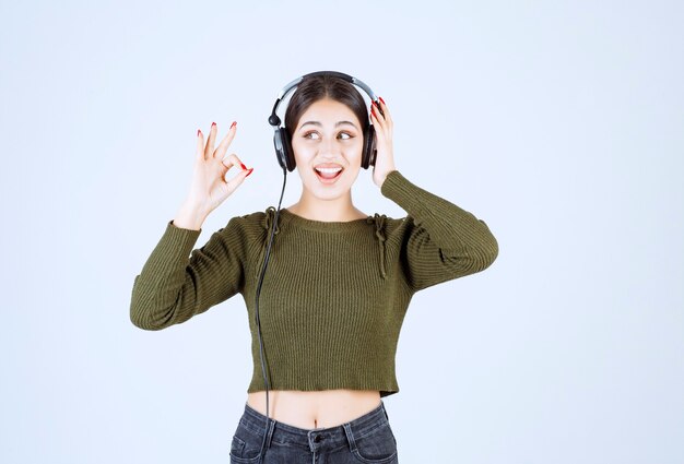 Portrait of young girl in headphones listening to music and giving ok sign.