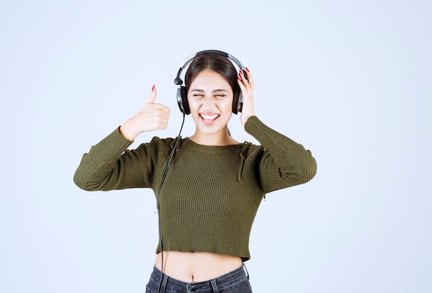 Portrait of young girl in headphones listening to music and giving thumbs up.