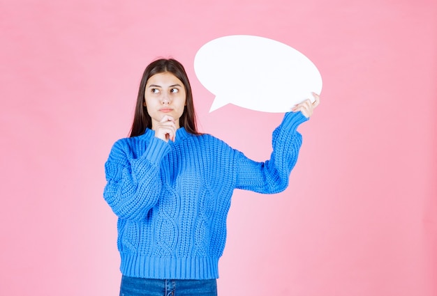 Portrait of a young girl holding blank speech bubble on pink.