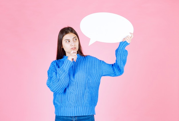 Portrait of a young girl holding blank speech bubble on pink.