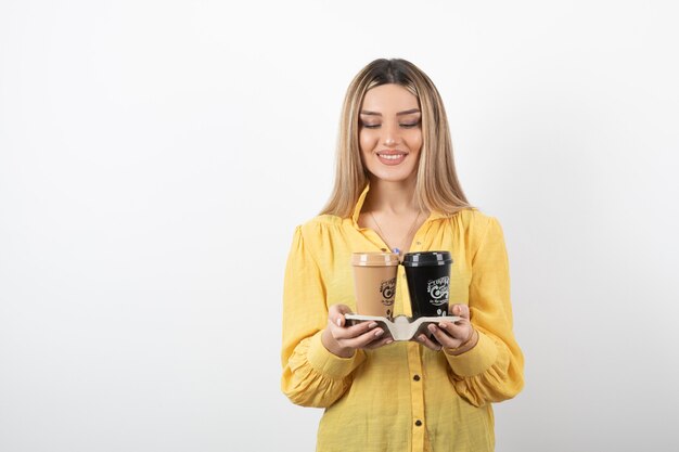 Portrait of young girl holding cups of coffee while smiling.