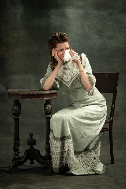 Портрет молодой девушки в образе средневековой королевской особы в платье в стиле ренессанс, пьющей кофе на темном фоне