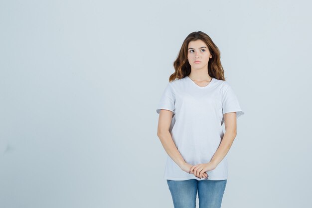 Portrait of young girl keeping hands in front of her in white t-shirt and looking pensive front view