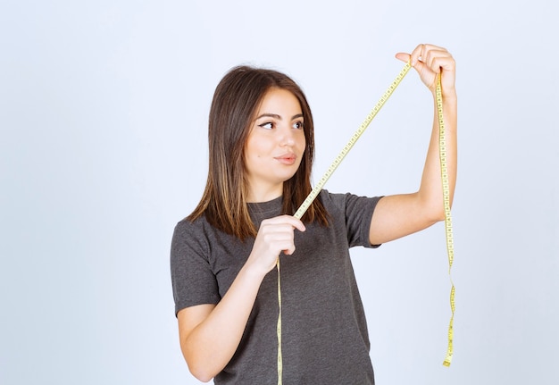 Portrait of a young girl looking at a measuring tape isolated over white background.