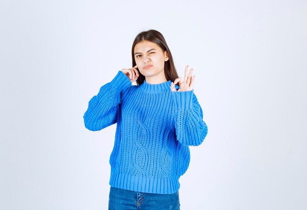 Portrait of a young girl model coning her ear and showing ok gesture .