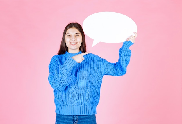 Portrait of a young girl pointing at a blank speech bubble .