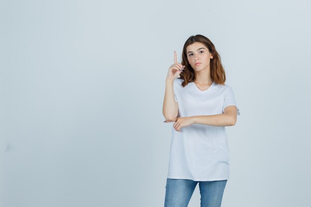 Portrait of young girl pointing up in white t-shirt and looking sensible front view