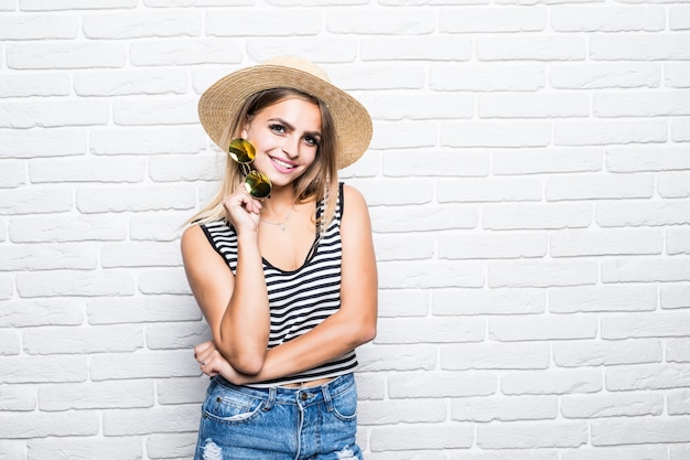 Portrait young girl posing in straw hat enjoying summer while standing on white brick wall