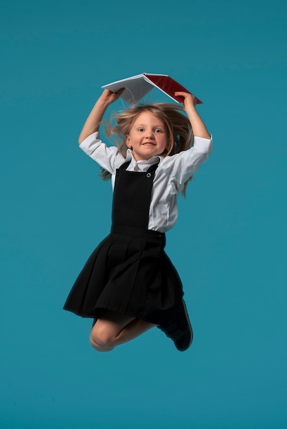 Free photo portrait of young girl student in school uniform jumping mid-air