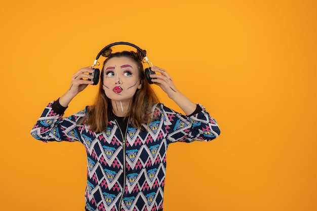 Portrait of young girl wearing creative makeup and listening music on headohones. High quality photo