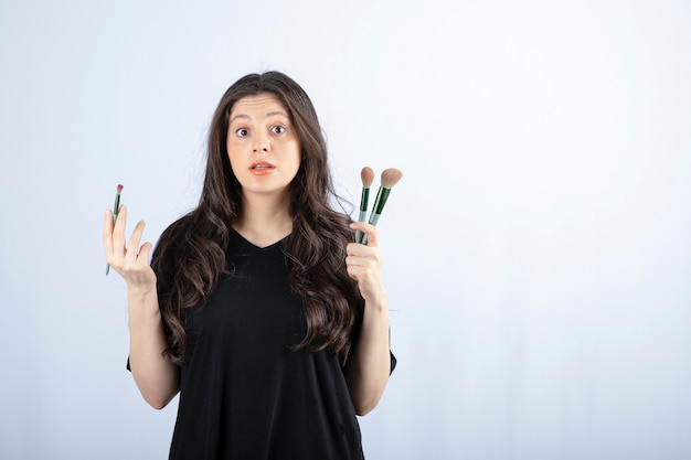 Ritratto di giovane ragazza con spazzole cosmetiche che guarda l'obbiettivo su bianco.