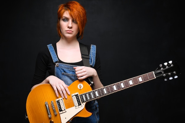 Ritratto di giovane ragazza con la chitarra su sfondo nero.