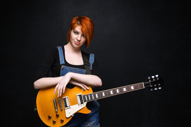 黒の背景上のギターを持つ若い女の子の肖像画。