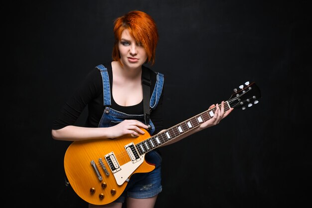 Portrait of young girl with guitar over black background.