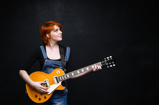 Portrait of young girl with guitar over black background.