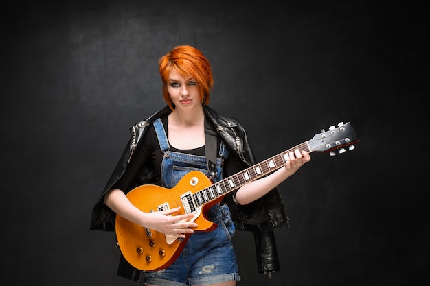 Portrait of young girl with guitar over black background.