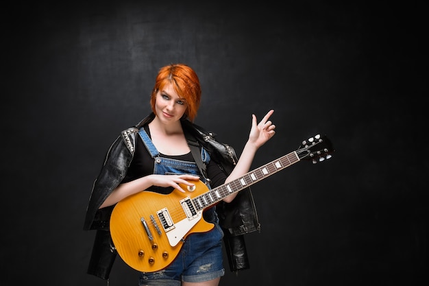 Portrait of young girl with guitar over black background.