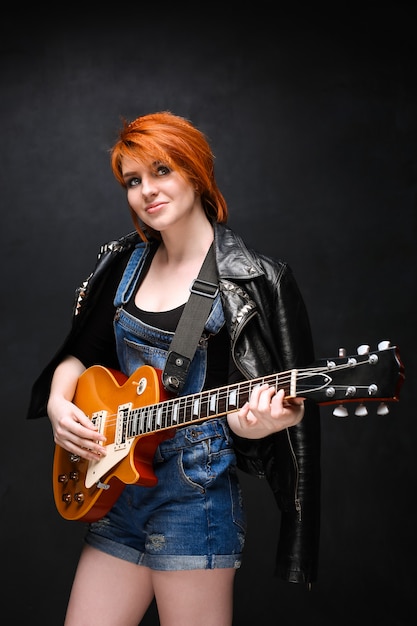 Портрет молодой девушки с гитарой на черном фоне.