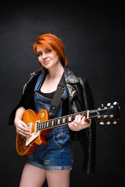 Портрет молодой девушки с гитарой на черном фоне.