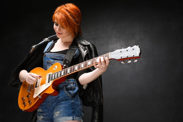 Ritratto di giovane ragazza con la chitarra su sfondo nero.