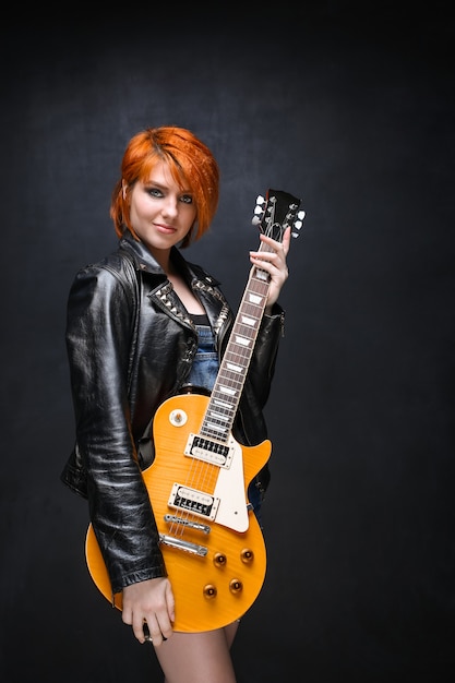 Portrait of young girl with guitar over black background.