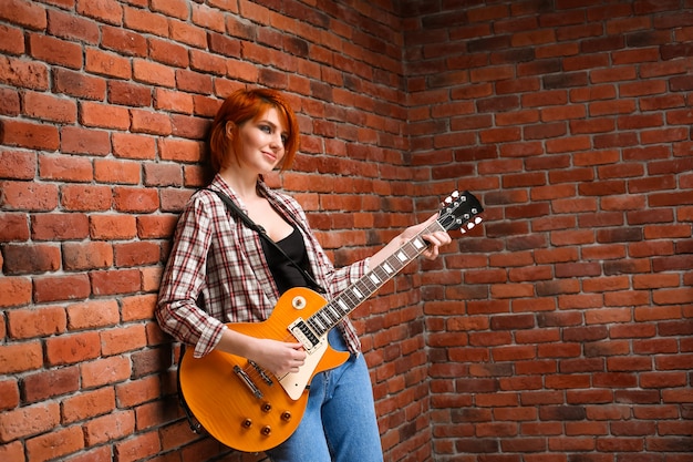 Portrait of young girl with guitar over brick background.