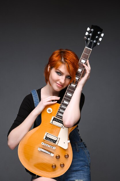 Portrait of young girl with guitar over grey background.