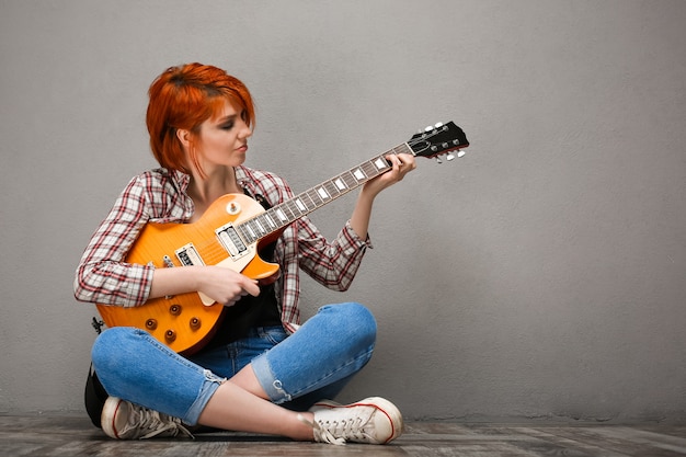 Portrait of young girl with guitar over grey background.