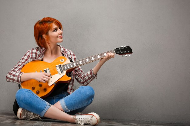 Portrait of young girl with guitar over grey background.