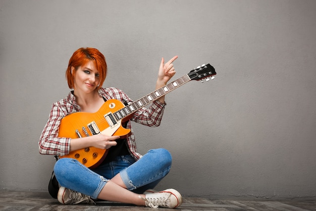 Portrait of young girl with guitar over grey background.