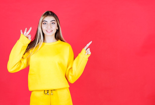 Free photo portrait of young girl in yellow outfit standing on red wall