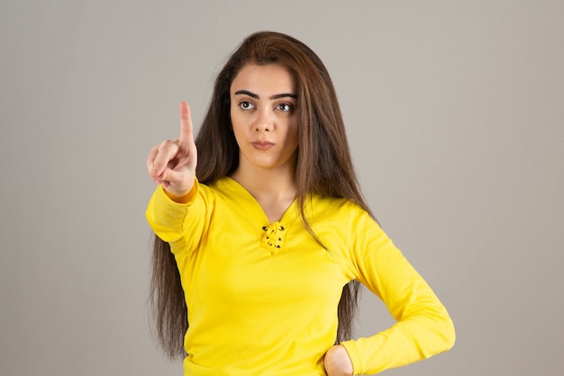 Portrait of young girl in yellow top looking and looking on gray wall.