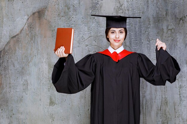 Portrait of young graduate student with book standing against wall. High quality photo