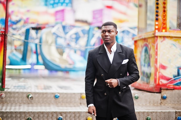 Портрет молодого и красивого афроамериканского бизнесмена в костюме позирует на фоне аттракционов карусели