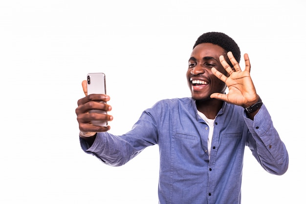 Portrait of young handsome African American man using smartphone to take selfie pictures and smiling standing against white wall