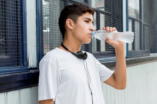 Ritratto di giovane ragazzo bello che beve acqua fredda che sta vicino al raccordo ondulato del ferro