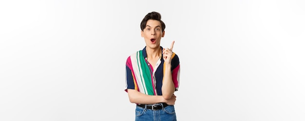 Portrait of young handsome guy having an idea raising finger and saying suggestion standing over white background