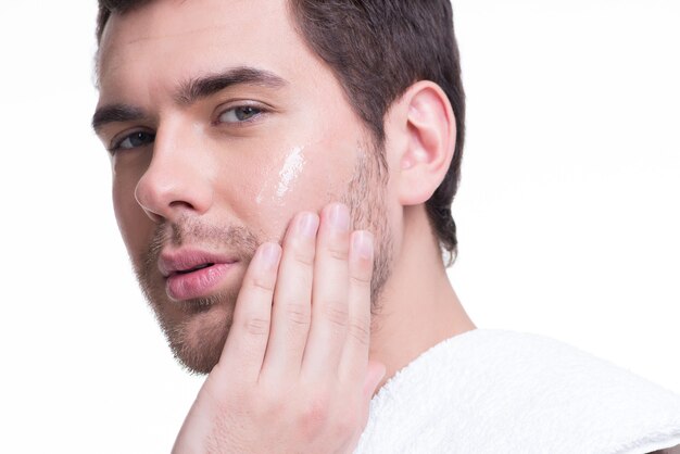 Portrait of young handsome man applying cream lotion on face - isolated on white.