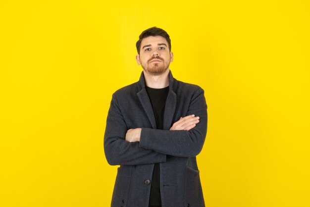 Portrait of young handsome man crossed his arms on a yellow.