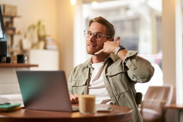 Portrait of young handsome man in glasses businessman working in cafe sitting with laptop showing