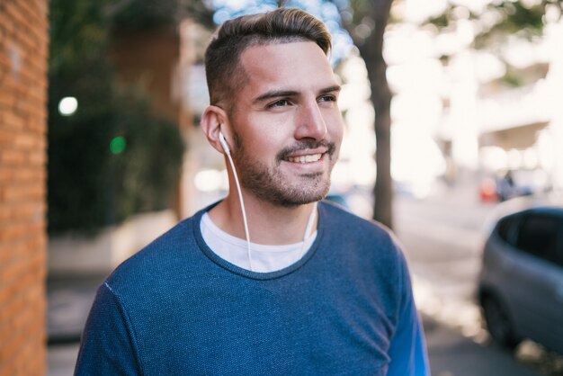 Портрет молодого красивого человека, слушающего музыку с наушниками на открытом воздухе на улице. Городская концепция.