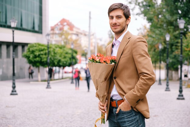 バラの花束を持って笑っている若いハンサムな男の肖像