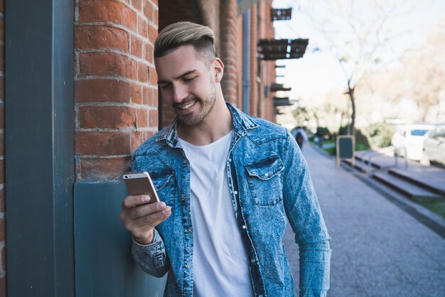 通りで屋外に彼の携帯電話を使用して若いハンサムな男の肖像画。コミュニケーションの概念。